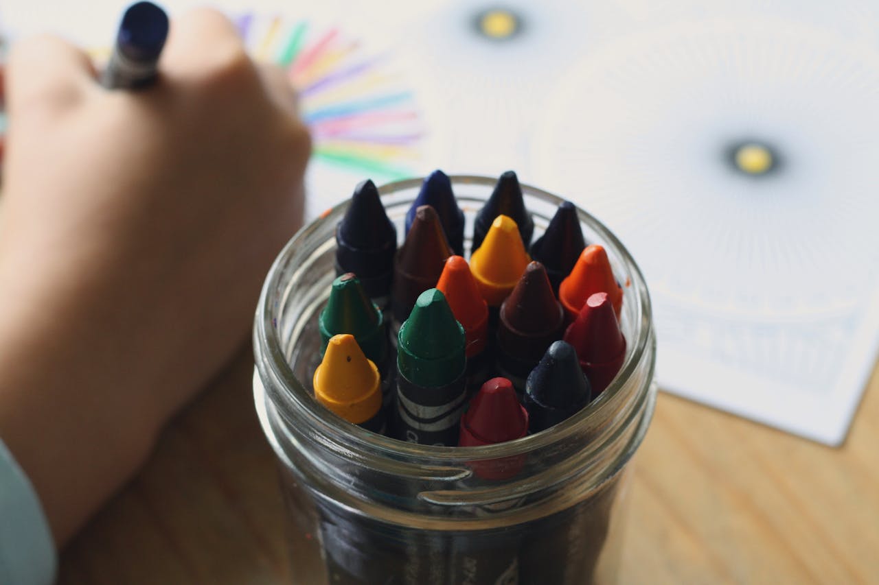 A child coloring with crayons in a jar, showcasing creativity and fun in art activities.