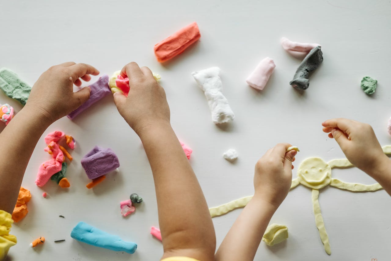 Children engaged in creative clay play, forming shapes and exploring colors on a white table.