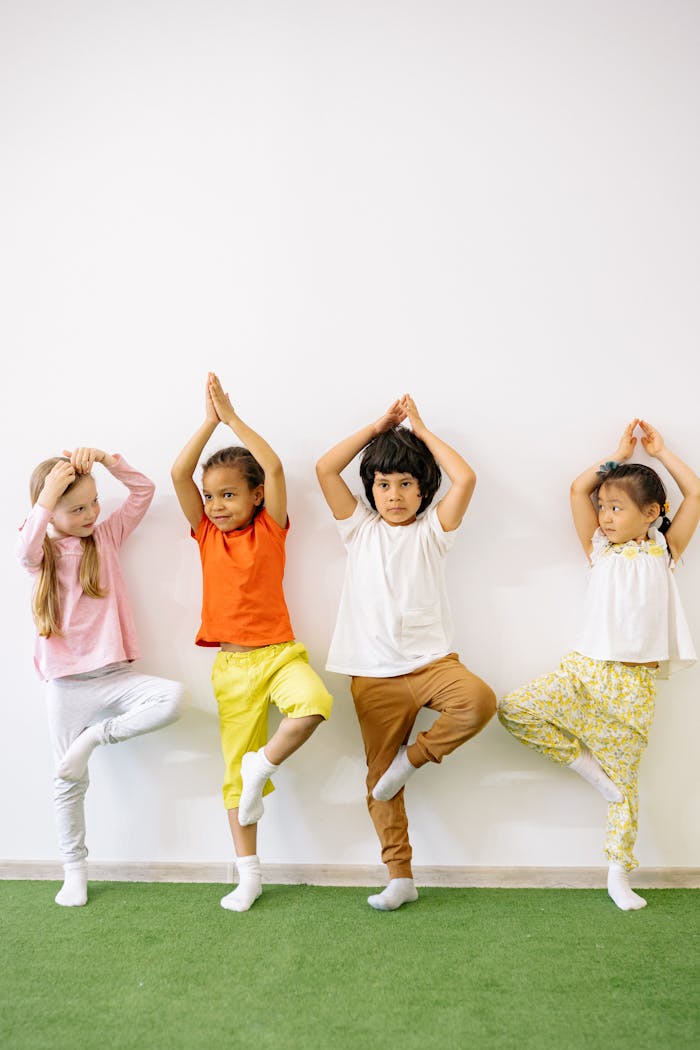 Four diverse children practicing yoga indoors, promoting fun and exercise in a learning environment.